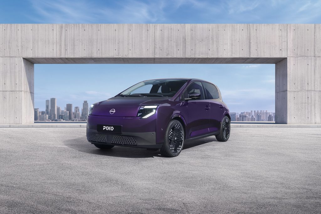 Three-quarter front view of a purple Nissan PIXO electric city car parked beneath a modern concrete structure, with a city skyline in the background.